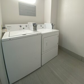 Een wasruimte met Whirlpool wasmachines en drogers, een bord met richtlijnen voor gastenwas, en een wandlamp.