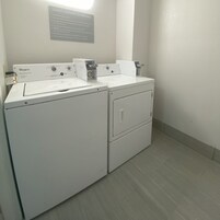 Un área de lavandería con lavadoras y secadoras Whirlpool, un cartel con indicaciones para huéspedes sobre el uso de la lavandería, y una luz instalada en la pared.