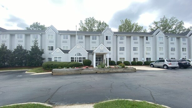 A multi-story hotel with a central entrance, parking area, and surrounding greenery. - Red Roof Inn Winston-Salem (Winston-Salem)