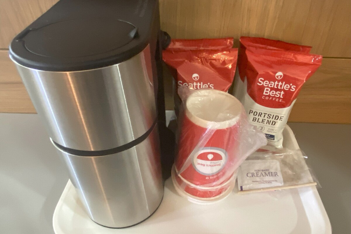 A stainless steel thermos, two packets of Seattle's Best coffee, a container of creamer, and a plastic cup on a white tray.