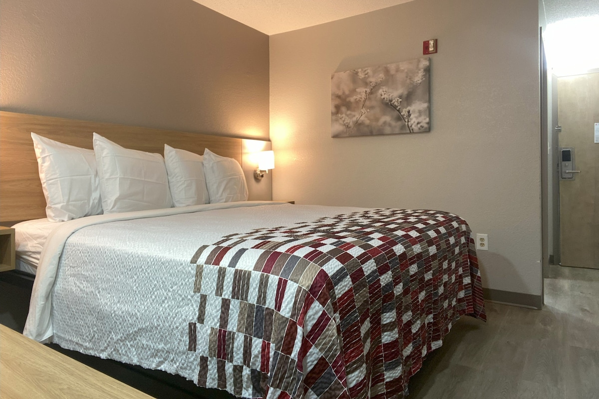A hotel room with a bed, a nightstand, a wall-mounted lamp, and a door.