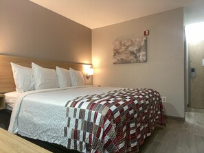 Een hotelkamer met een bed, nachtkastje, een wandlamp en een deur.