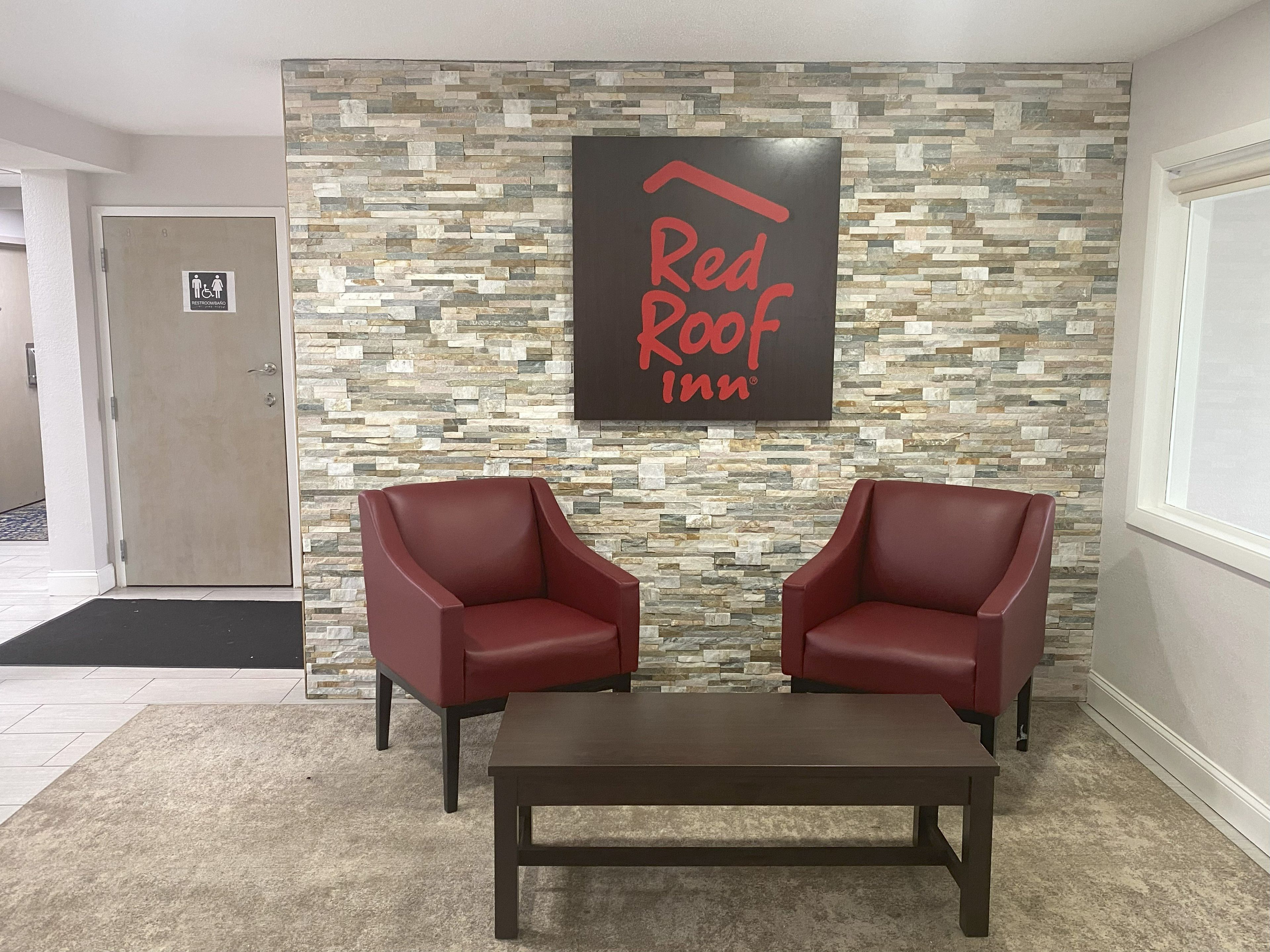 Zona de recepción de Red Roof Inn con pared de piedra, dos sillones de cuero rojo y una mesa de madera oscura.