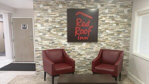 A Red Roof Inn reception area with a stone wall, two red leather chairs, and a dark wooden table. - Red Roof Inn Winston-Salem (Winston-Salem)