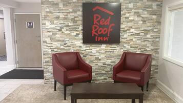 Zona de recepción de Red Roof Inn con pared de piedra, dos sillones de cuero rojo y una mesa de madera oscura.
