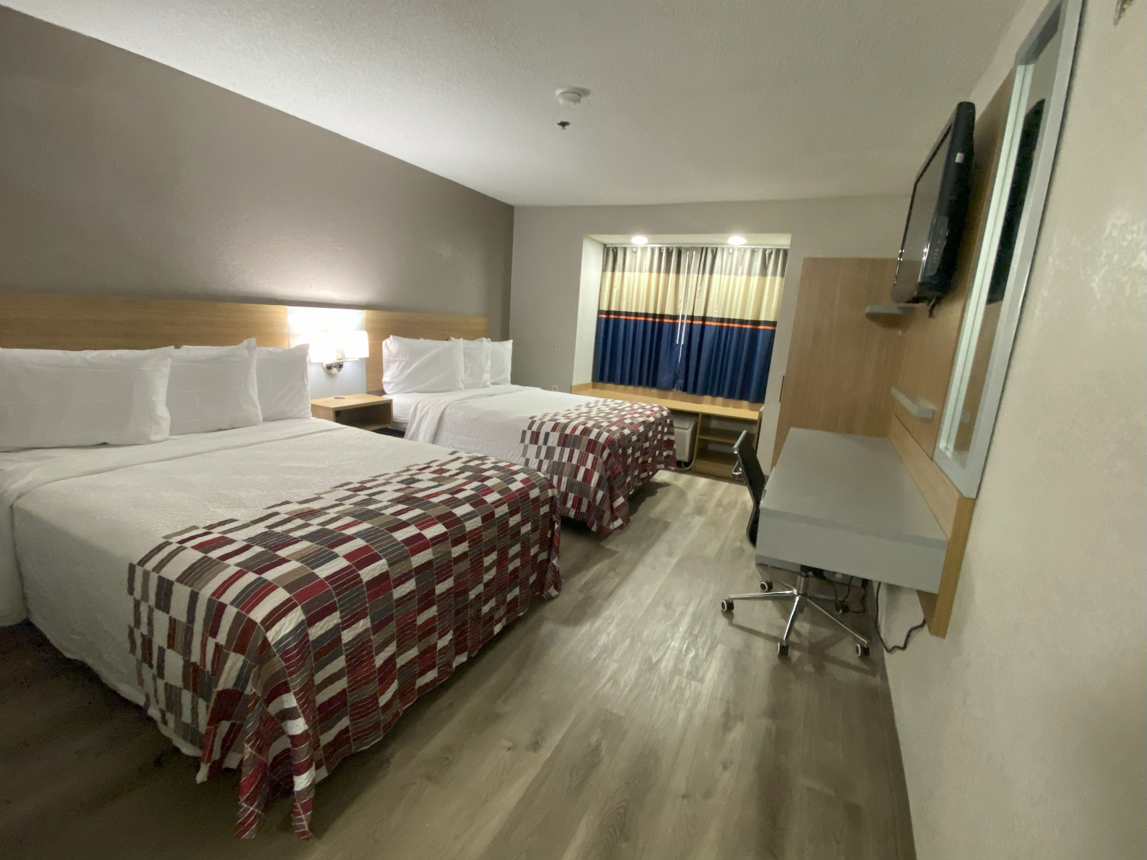 A hotel room with two beds, a desk, a chair, a TV, and a window with curtains.