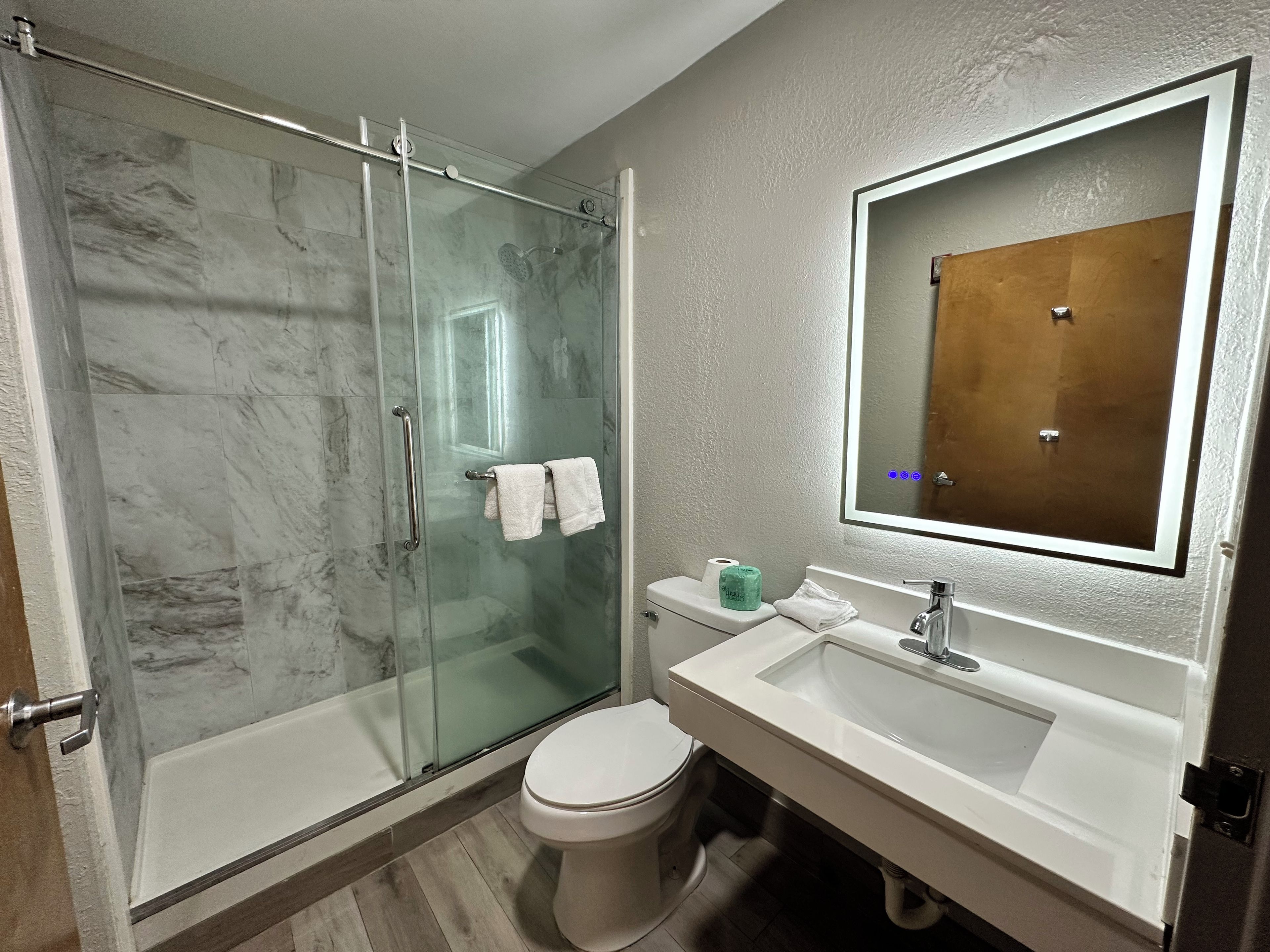 Un baño con ducha de vidrio, inodoro blanco, lavabo con espejo y perchero para toallas.