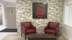 A Red Roof Inn reception area with a stone wall, two red leather chairs, and a dark wooden table. - Red Roof Inn Winston-Salem (Winston-Salem)