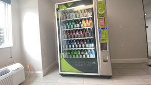 A vending machine stocked with various beverages in a room with a window and a wall-mounted air conditioner. - Red Roof Inn Winston-Salem (Winston-Salem)