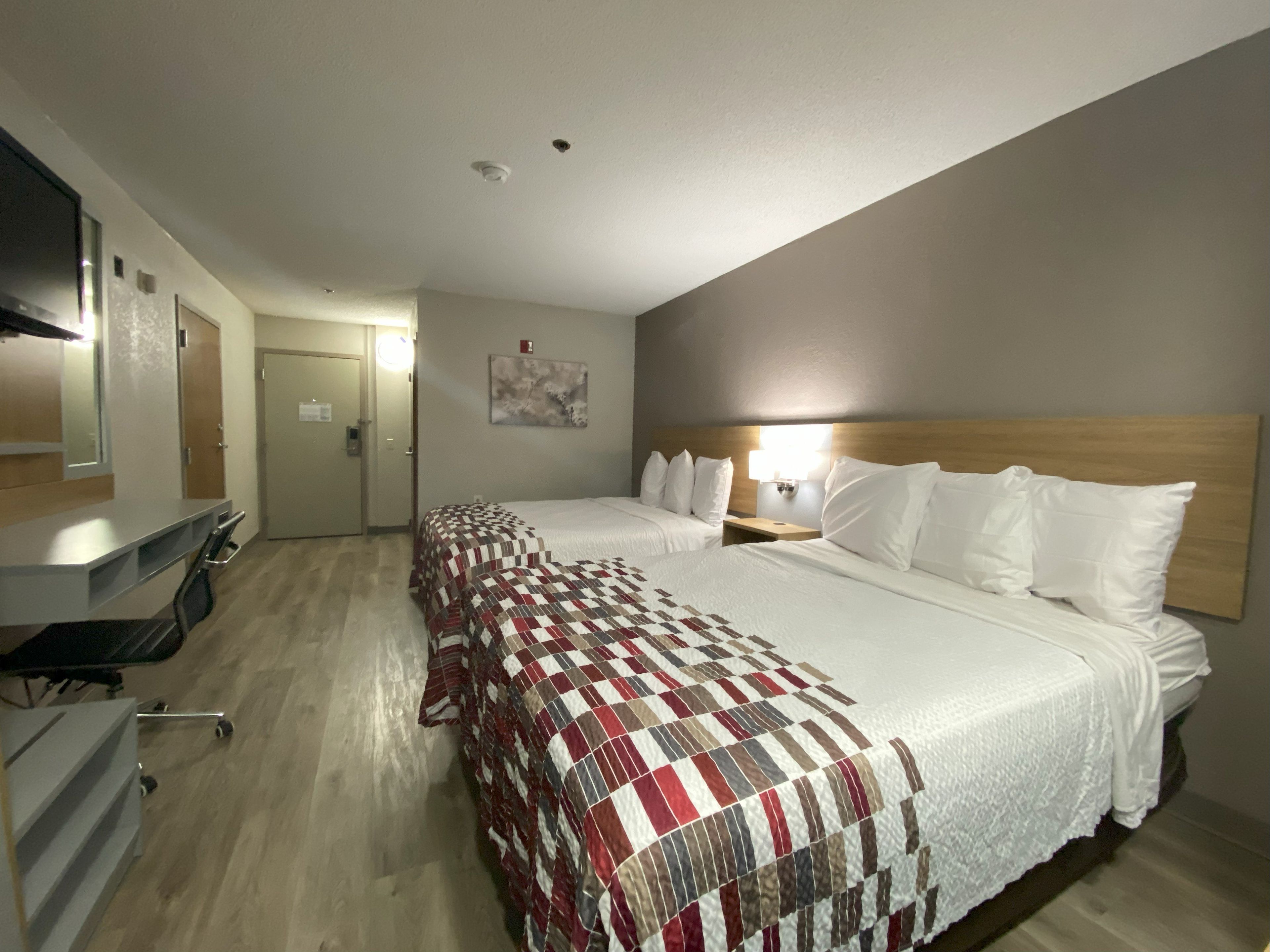 A hotel room with two beds, a desk, a chair, and a mirror.