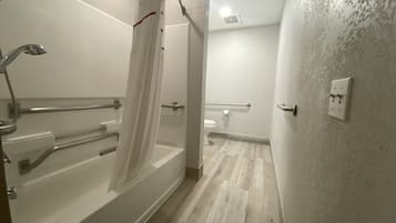 A bathroom with a bathtub, shower, toilet, and handrails.