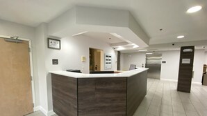 A reception area with a dark wood reception desk, a door, and a view into a hallway with a refrigerator and a door. - Red Roof Inn Winston-Salem (Winston-Salem)