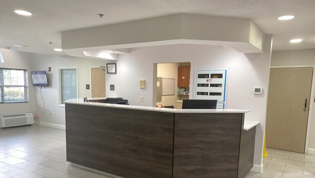 A reception area with a dark wood reception desk, a white wall-mounted TV, and a door with a sign. - Red Roof Inn Winston-Salem (Winston-Salem)