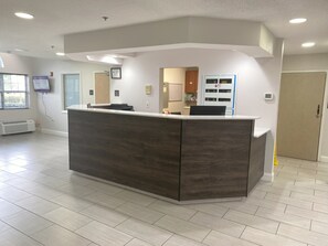 A reception area with a dark wood reception desk, a white wall-mounted TV, and a door with a sign. - Red Roof Inn Winston-Salem (Winston-Salem)