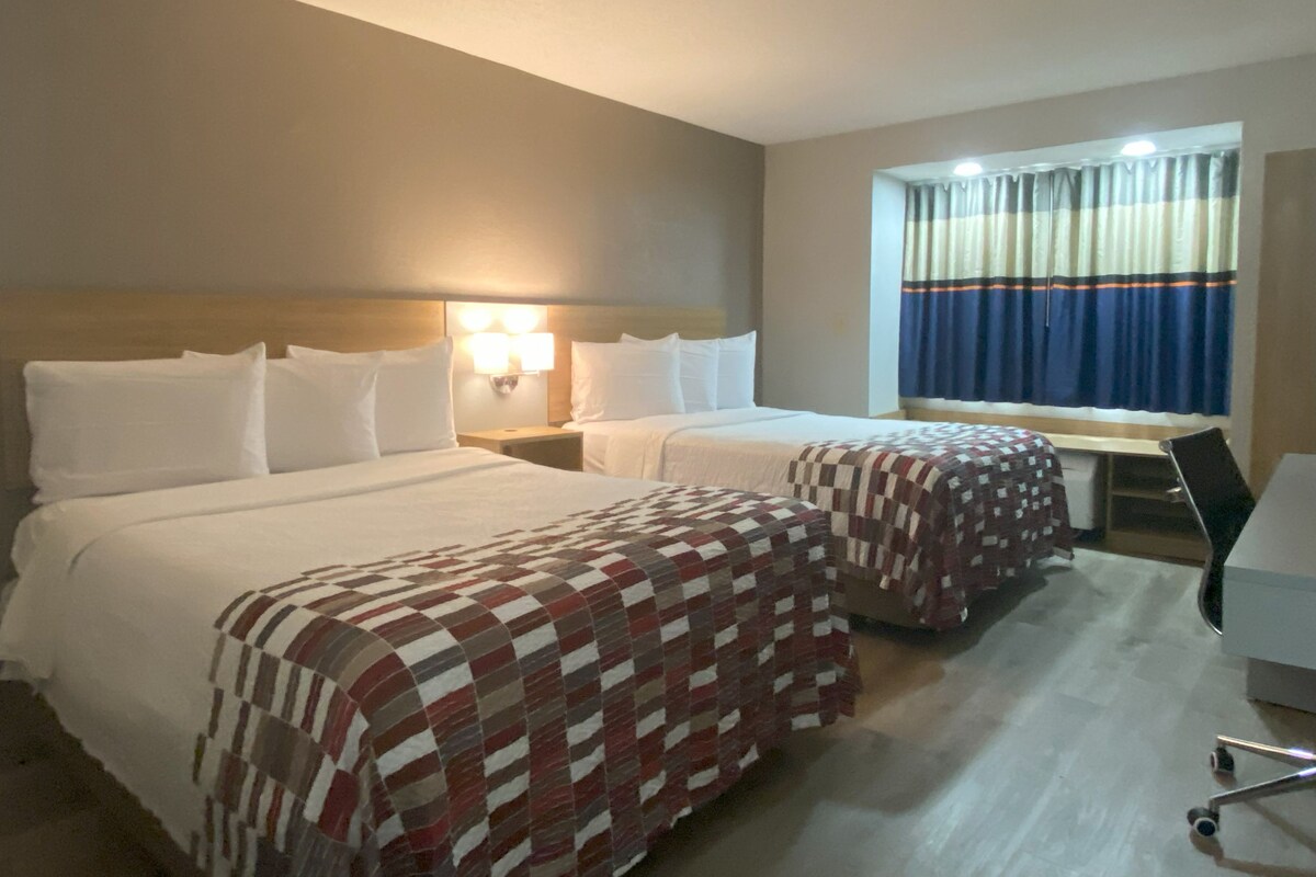 A hotel room with two beds, a desk, and a window with curtains.