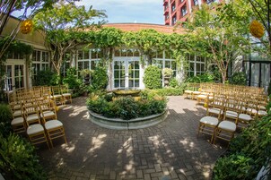 Un patio exterior con una distribución circular de asientos, una fuente en el centro y follaje circundante.