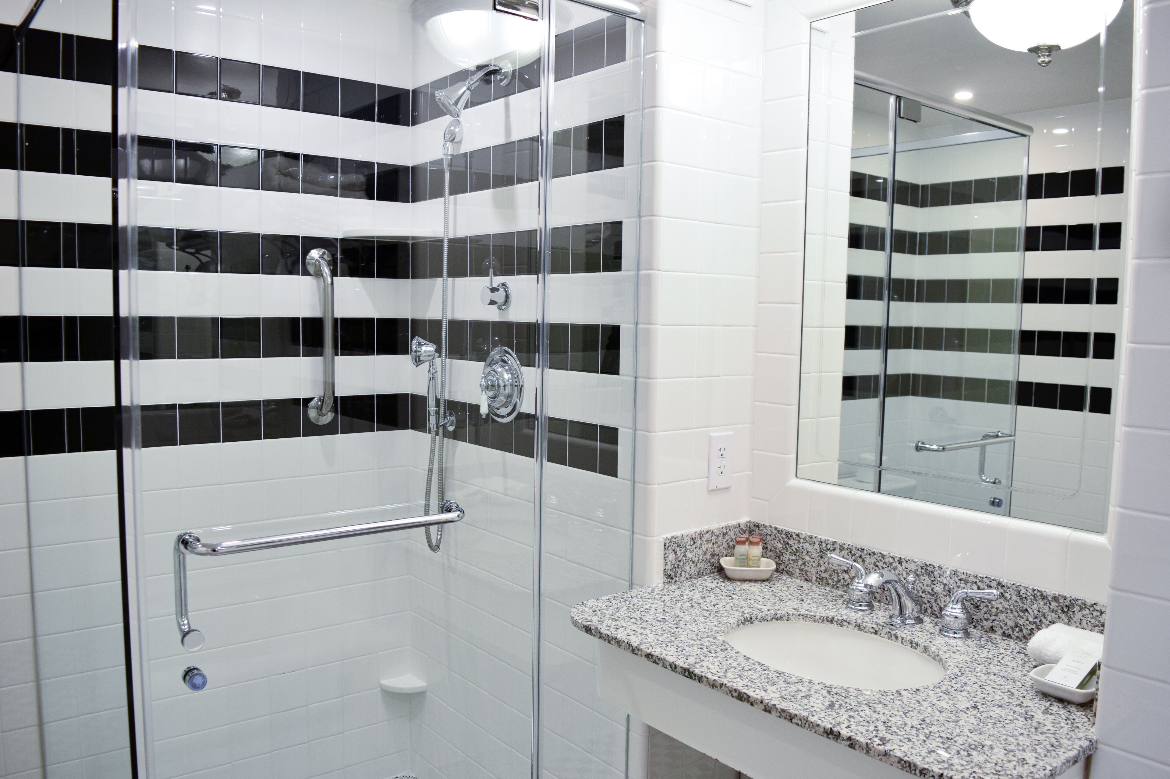 Un baño moderno con ducha de vidrio, lavamanos de granito y un espejo grande.