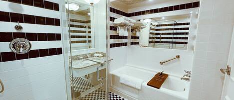 Un baño con piso a cuadros, ducha con cerramiento de vidrio, lavamanos con barra para toallas y bañera con bandeja de madera.