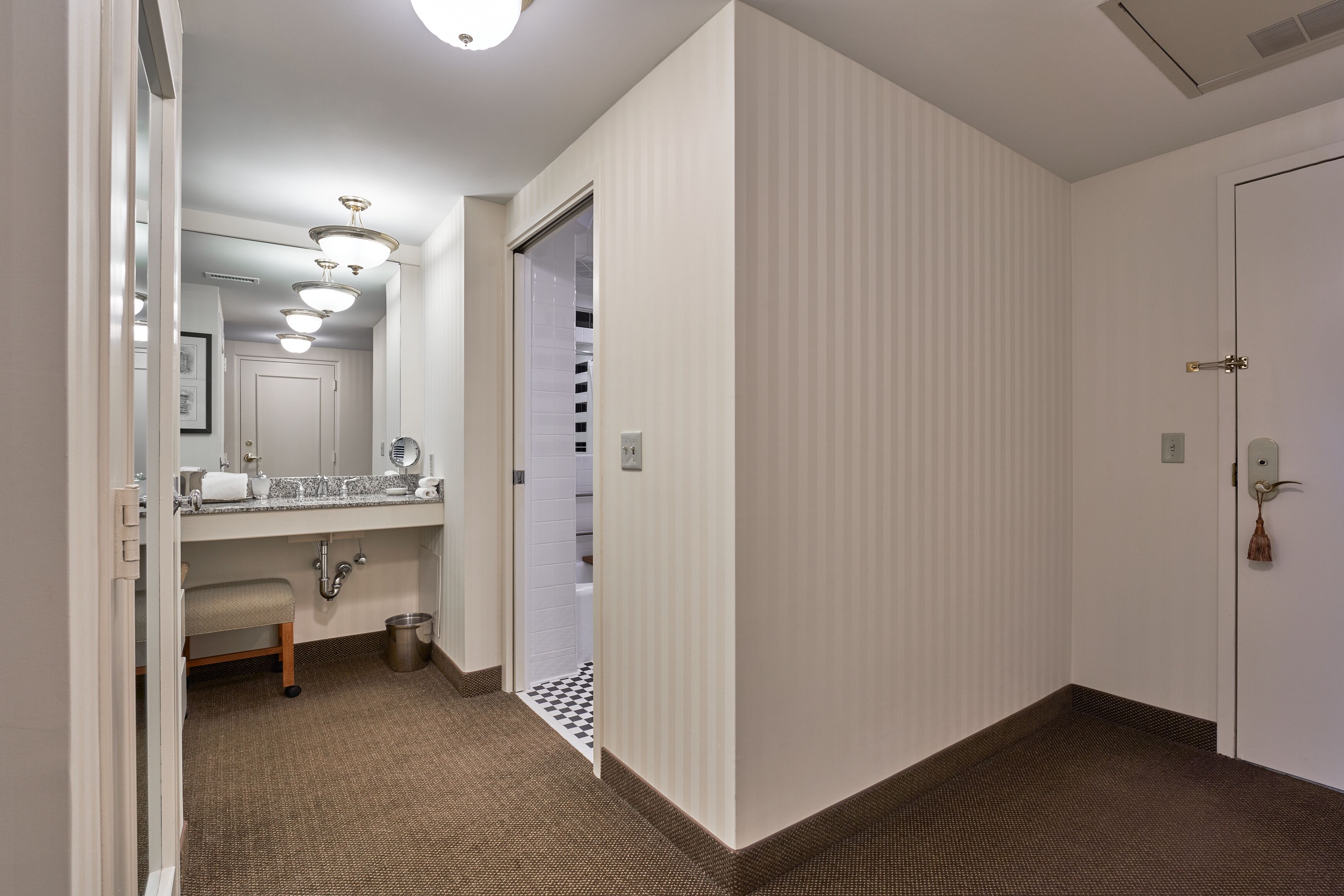 A hotel hallway with a bathroom featuring a sink, mirror, and towel rack.