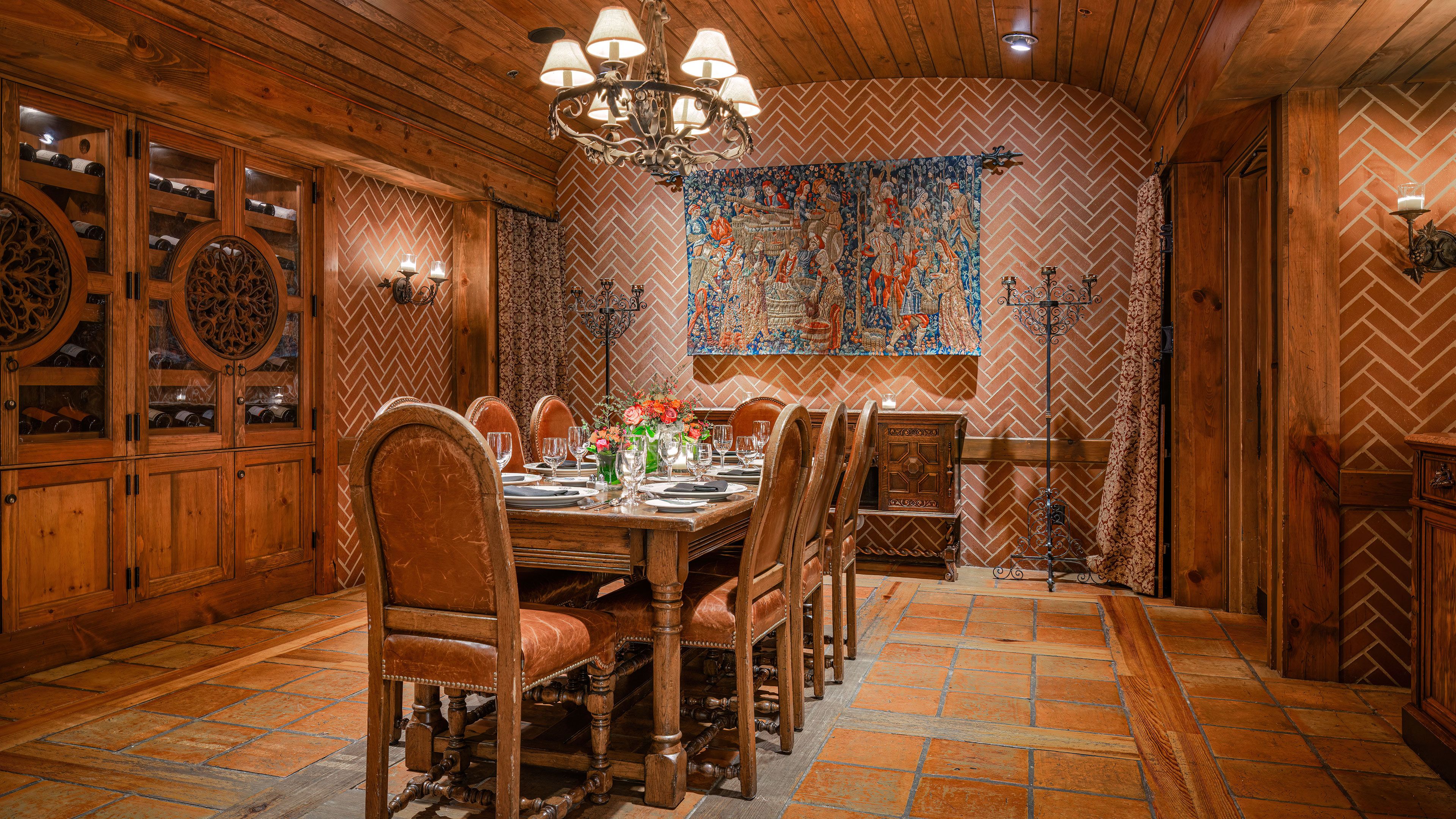 Un comedor con una mesa de madera dispuesta para seis personas, sillas alrededor y un tapiz decorativo grande en la pared.