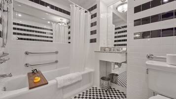 A modern bathroom with a bathtub, a shower, and a toilet. There are grab bars, a towel rack, and a small wooden tray with a rubber duck. The floor has a black and white checkered pattern.