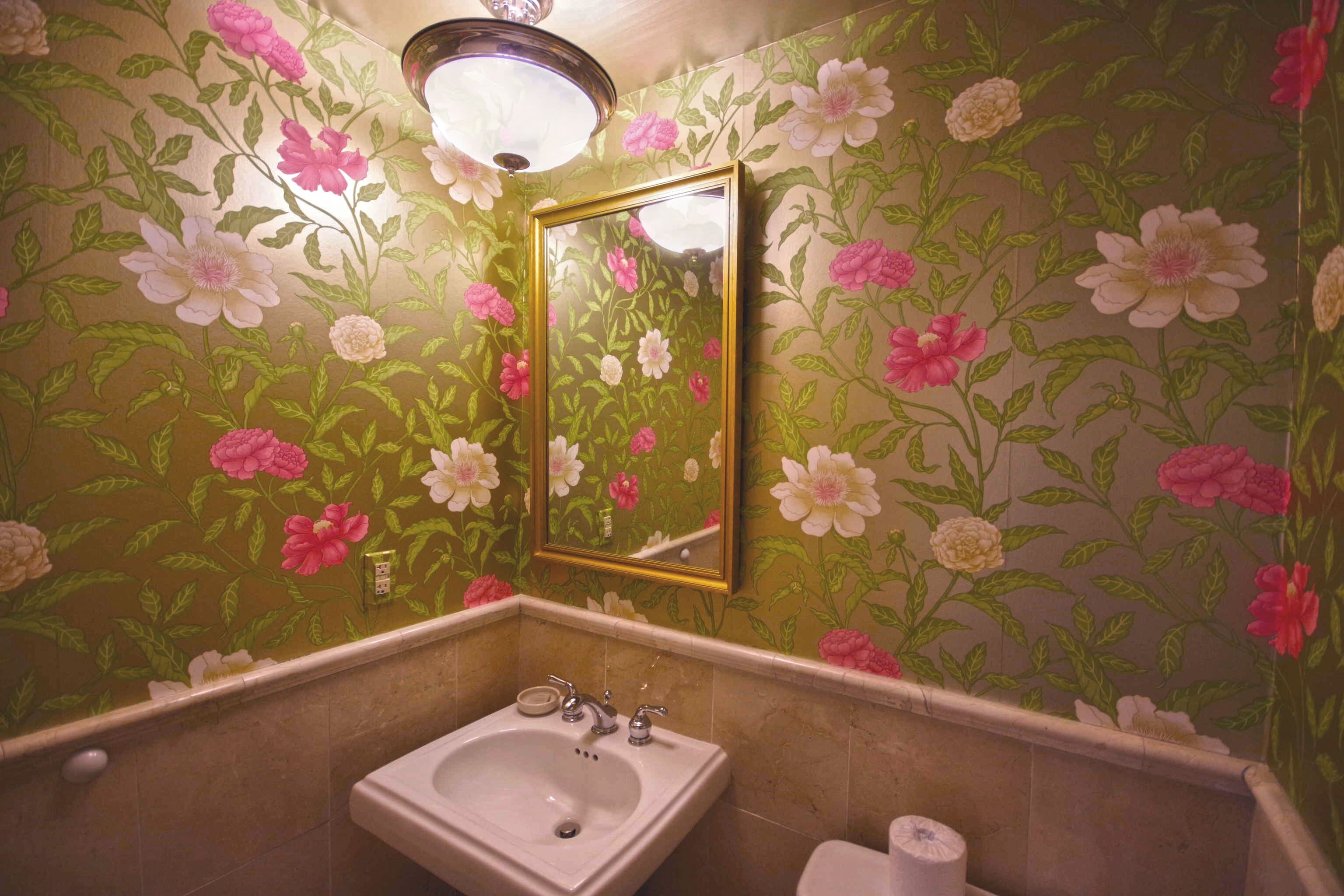 Et badeværelse med blomstret tapet, vask og spejl.