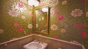 Un baño con papel tapiz floral, un lavamanos y un espejo.