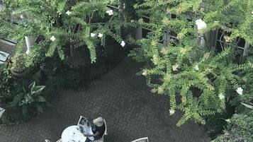 An outdoor patio area with brick flooring, surrounded by lush green plants and white flowering shrubs.
