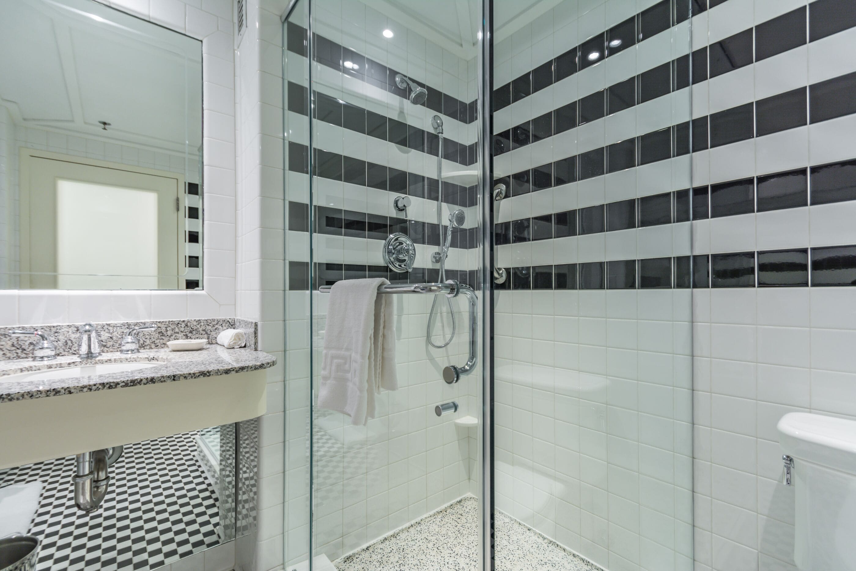 A modern bathroom with a glass-enclosed shower, a white sink with a marble countertop, and a checkered floor pattern.