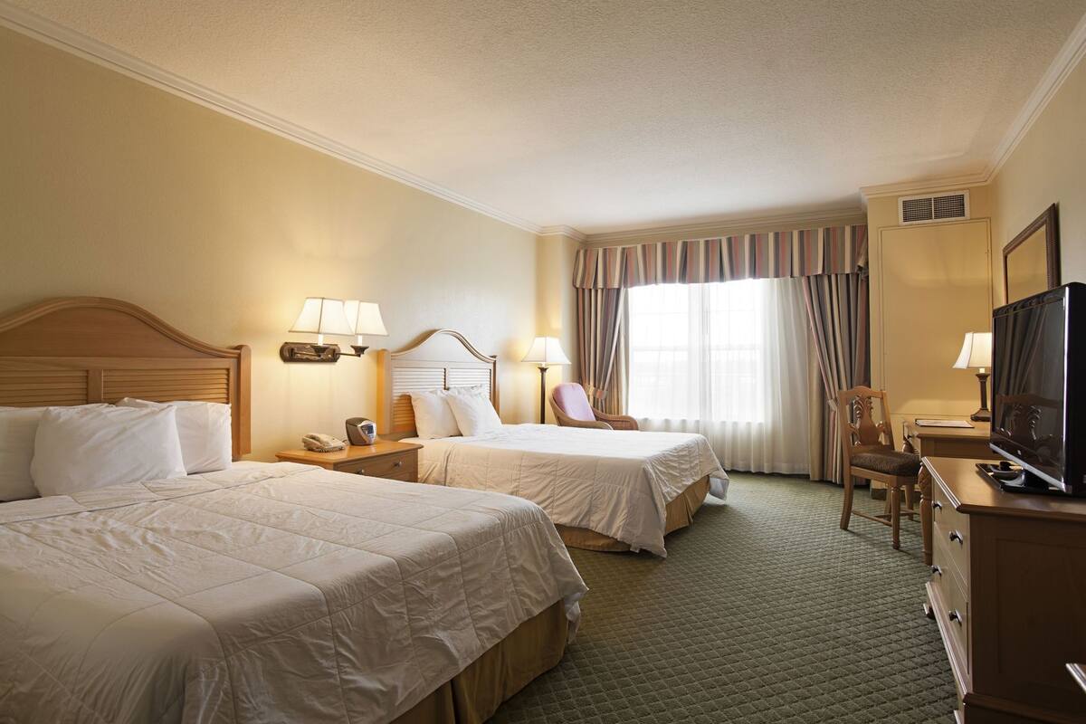 A hotel room with two beds, a desk with a television, a chair, and a window with curtains.