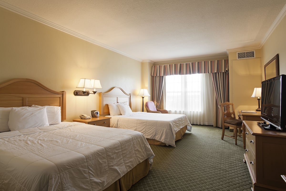 A hotel room with two beds, a television, a desk, and a chair.