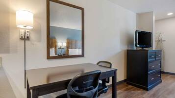 Habitación de hotel con escritorio, silla, televisor, cómoda y espejo.