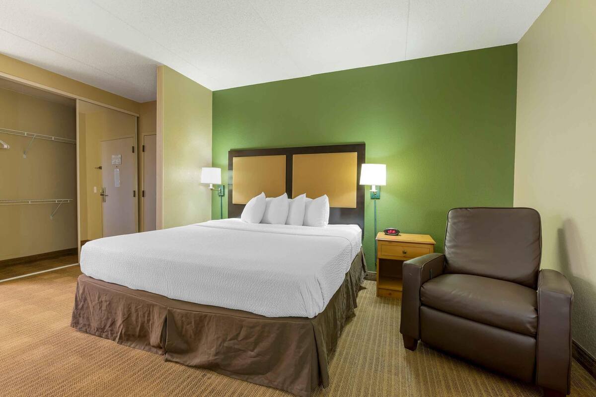 A hotel room with a large bed, two bedside lamps, a brown leather chair, and a green accent wall.
