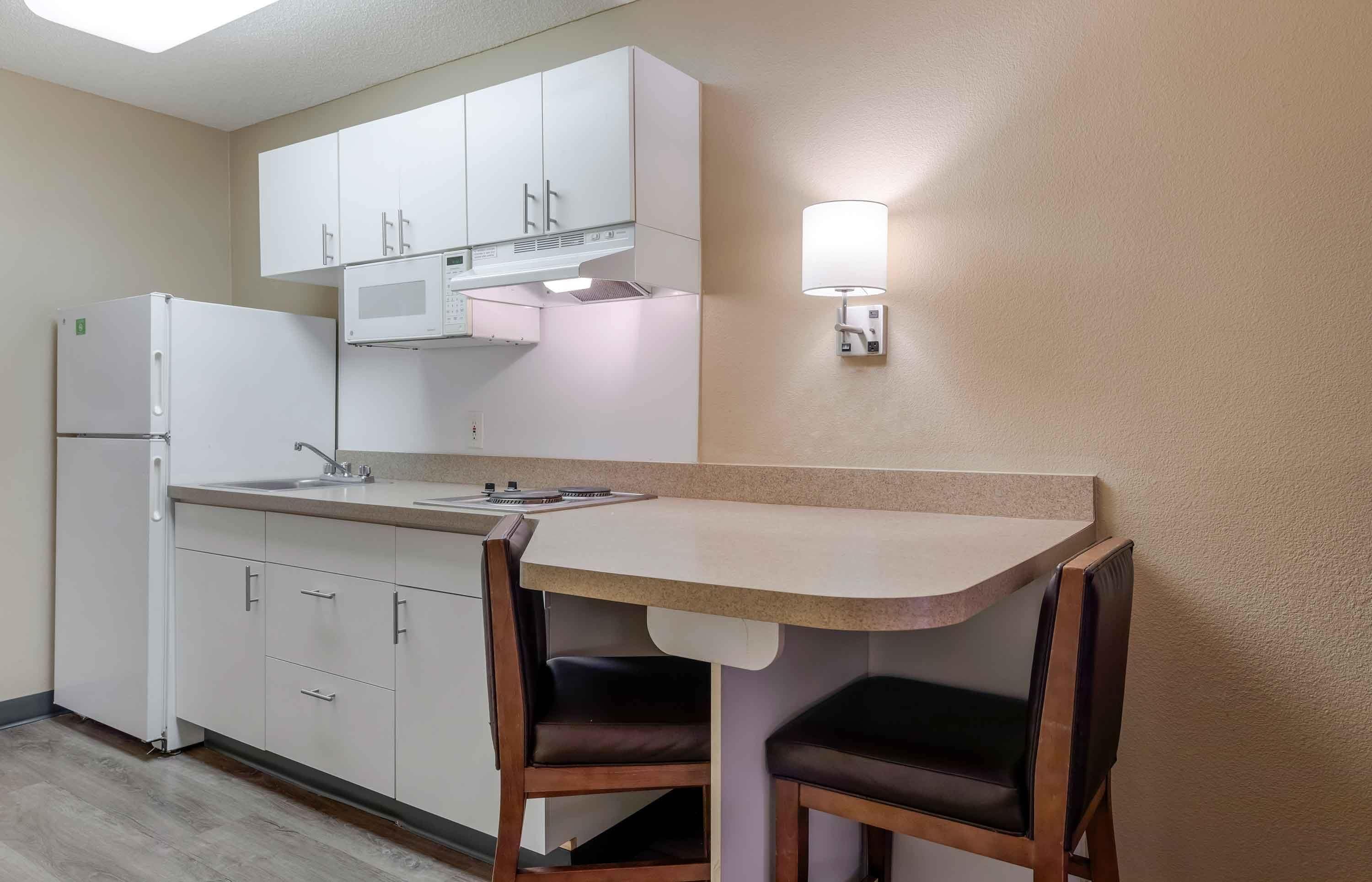 A compact kitchen with white cabinets, a microwave, a refrigerator, a sink, and a small dining area with two chairs.