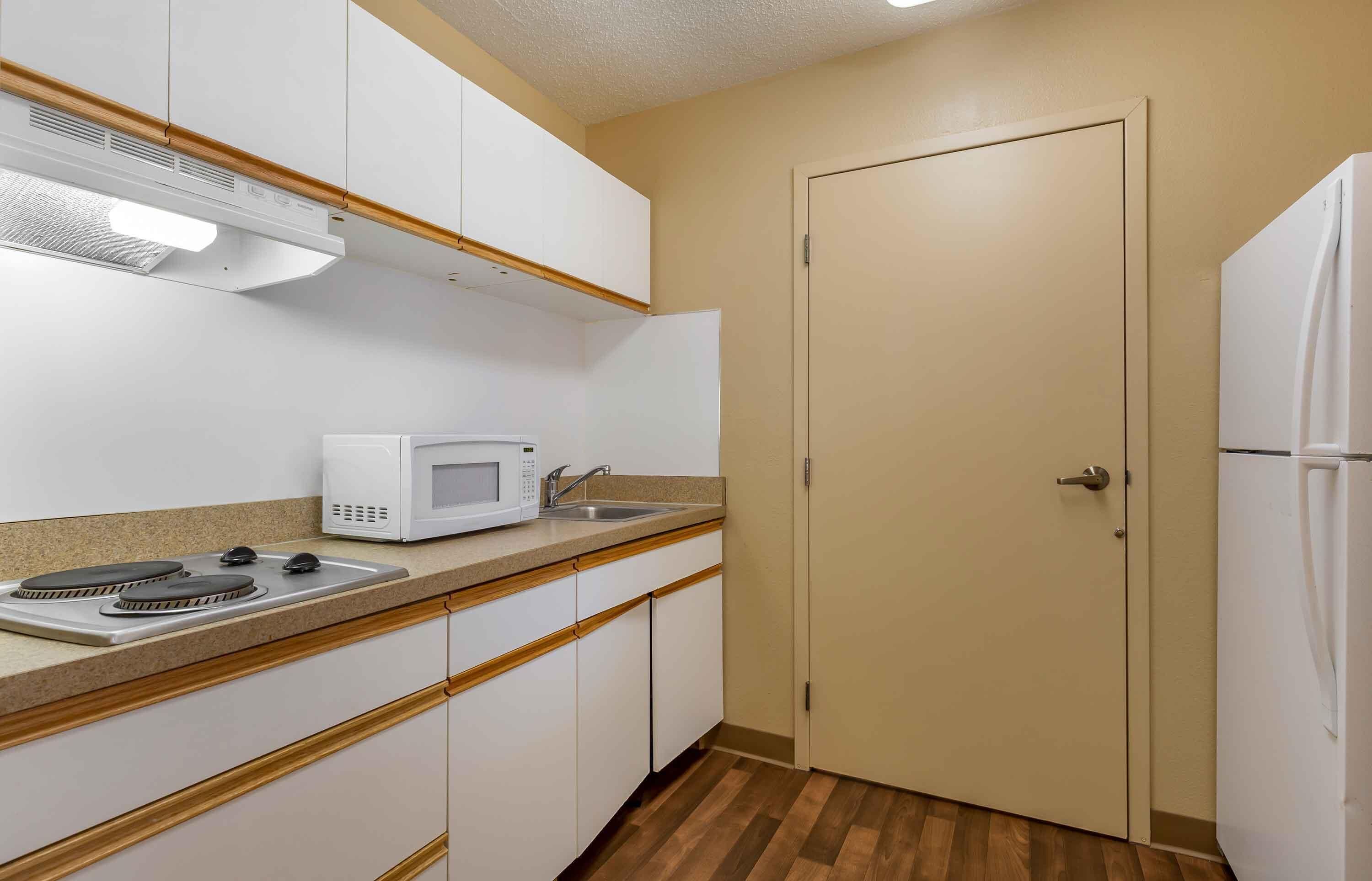 Una cocina compacta con armarios blancos, un microondas, estufa, fregadero y refrigerador.