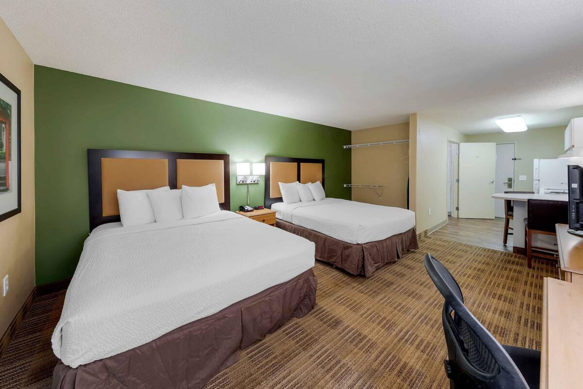 A hotel room with two beds, a desk, a chair, and a microwave.