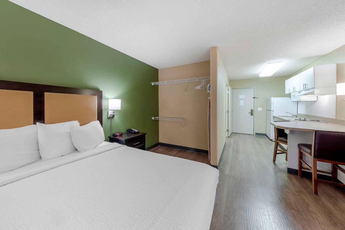 A hotel room with a bed, a desk, and a kitchenette.
