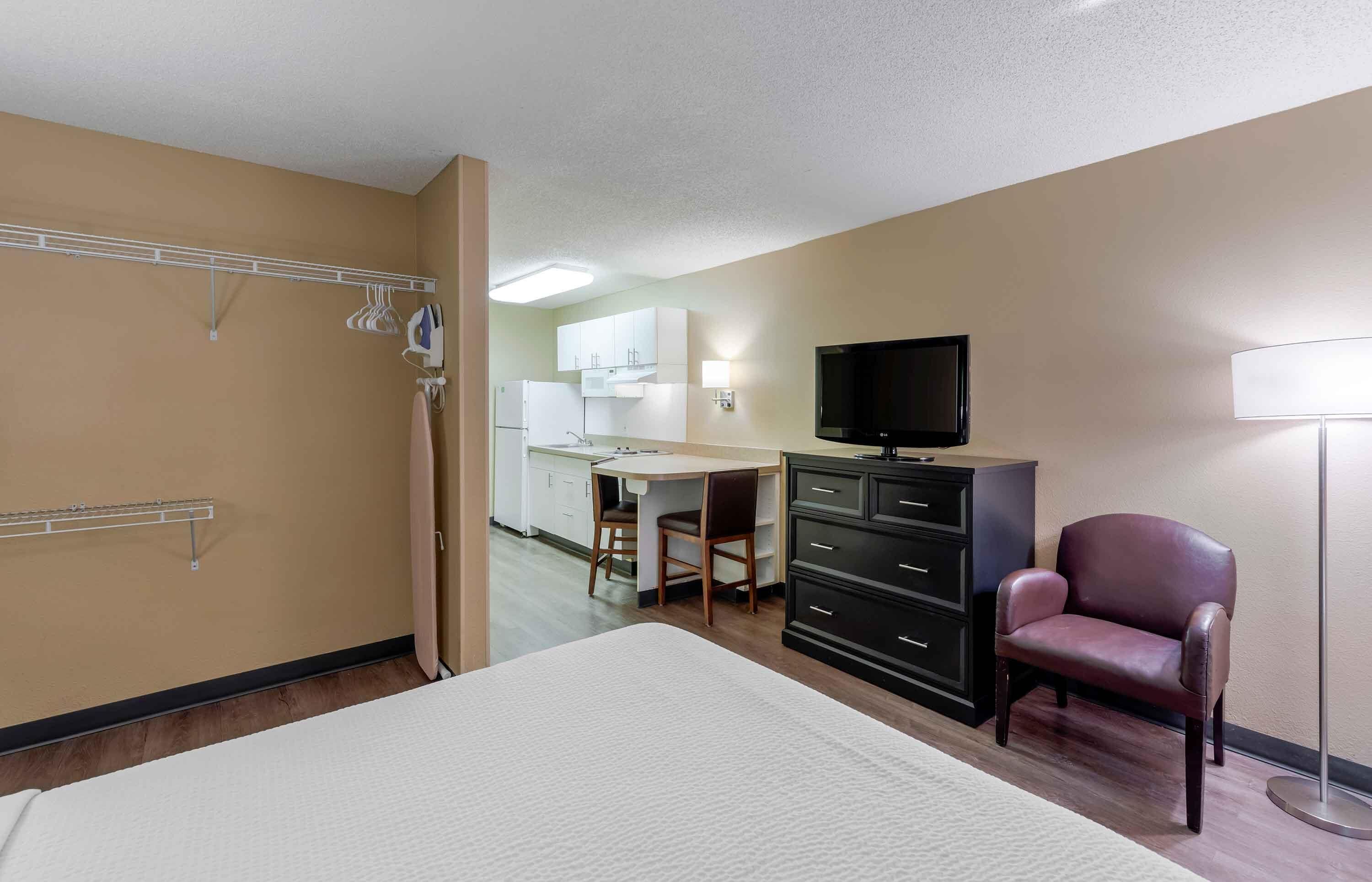 A hotel room with a bed, a desk with a chair, a television, a dresser, and a lamp.