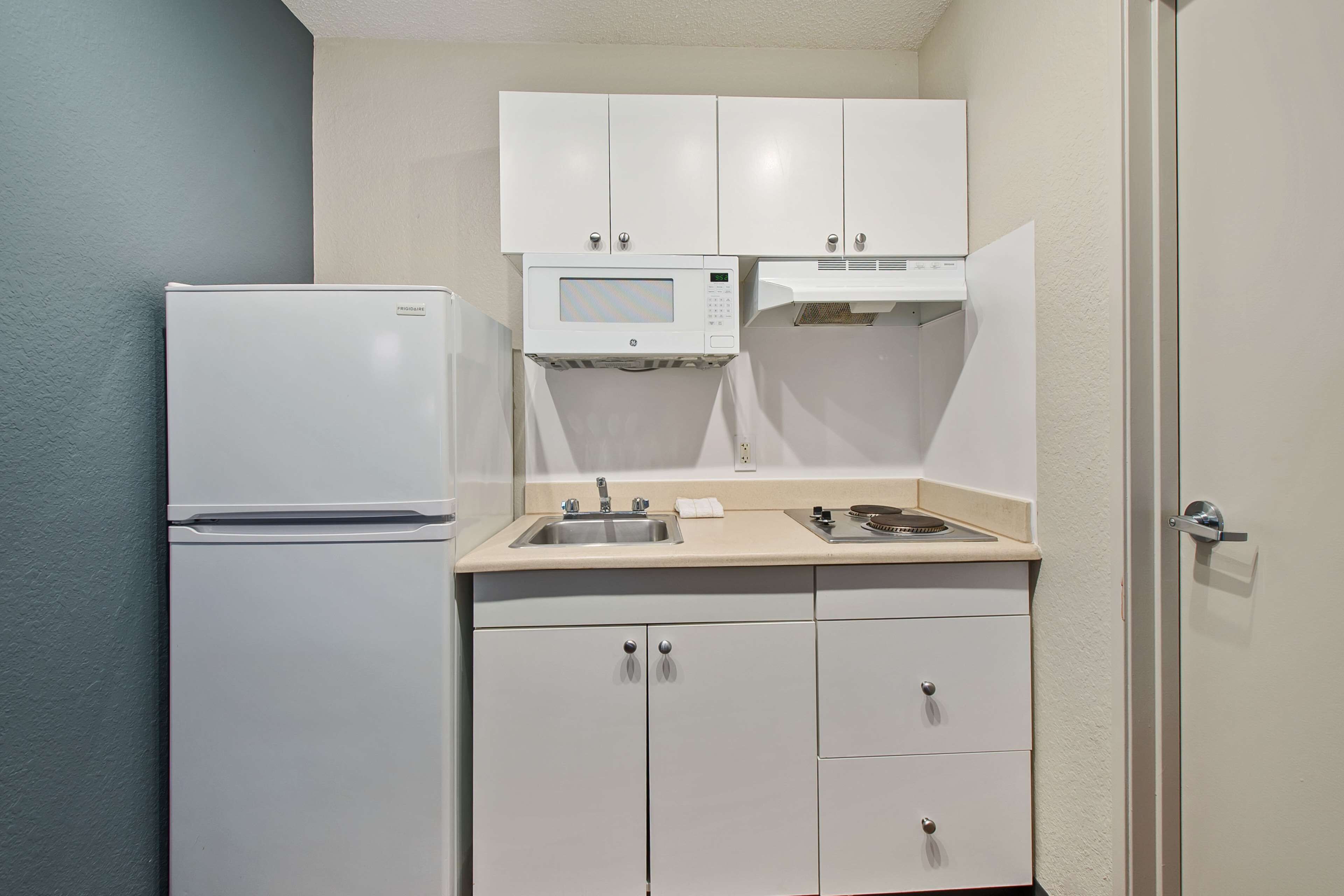 A compact kitchen with white cabinets, a refrigerator, a microwave, and a sink.
