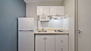 Una cocina compacta con armarios blancos, un microondas integrado y un refrigerador.