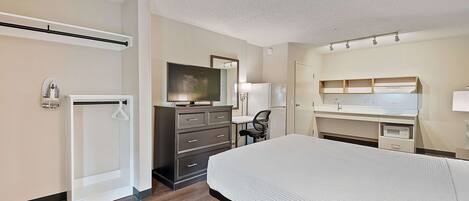 A hotel room with a bed, a desk, a chair, a television, a wardrobe, and a shower.
