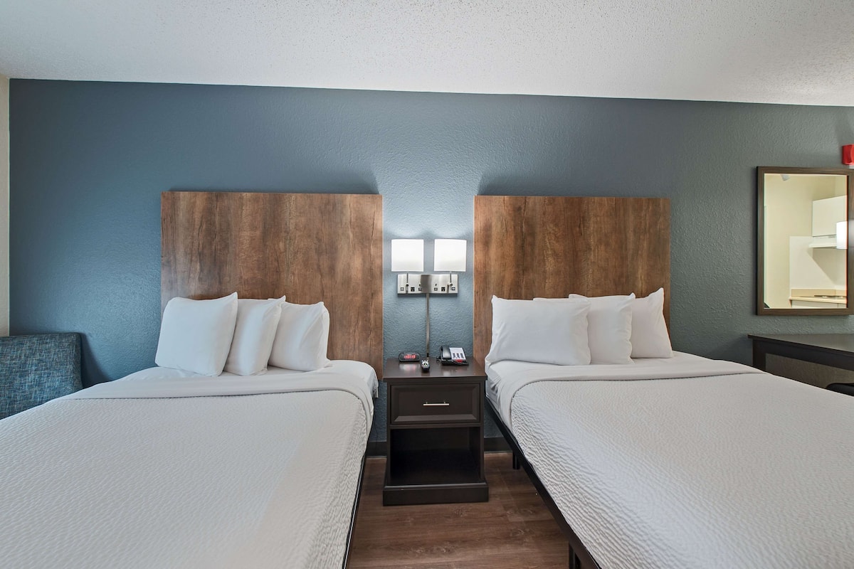 A hotel room with two beds, a nightstand with a lamp, and a mirror on the wall.