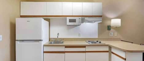 Een kleine keuken met witte kasten, een ingebouwde magnetron, een koelkast, een spoelbak en een klein aanrecht.
