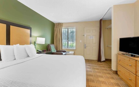A hotel room with a large bed, a desk with a lamp, a television, and a window with curtains.