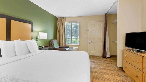 A hotel room with a large bed, a desk with a lamp, a television, and a window with curtains. - Extended Stay America Select Suites - Washington, DC - Sterling - Dulles (Sterling)