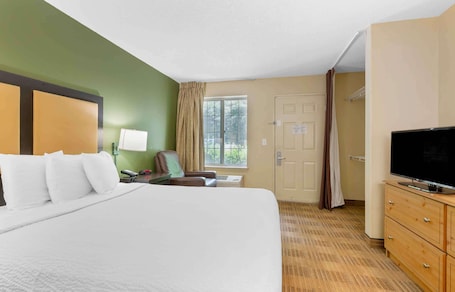 A hotel room with a large bed, a desk with a lamp, a television, and a window with curtains.