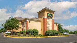 A Stay AmeriCa hotel with a beige facade, a prominent tower with a sign, and a parking lot with a few cars. - Extended Stay America Select Suites - Washington, DC - Sterling - Dulles (Sterling)