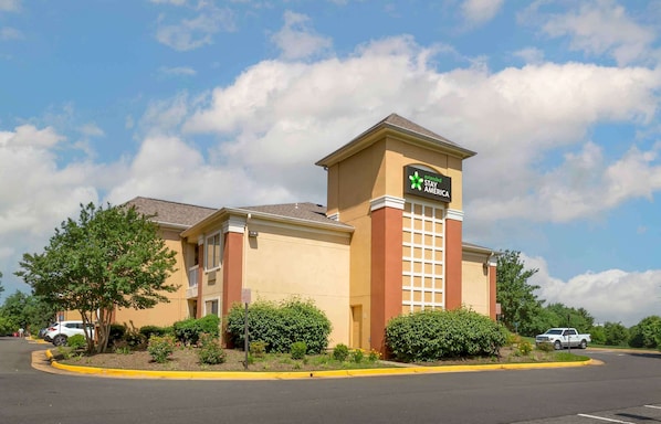 A Stay AmeriCa hotel with a beige facade, a prominent tower with a sign, and a parking lot with a few cars. - Extended Stay America Select Suites - Washington, DC - Sterling - Dulles (Sterling)