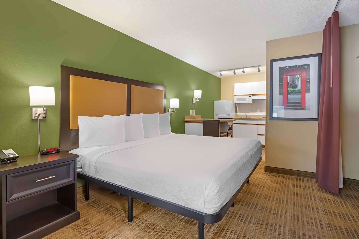 Une chambre d’hôtel comprenant un lit, une table de chevet, une lampe et un bureau avec une chaise.