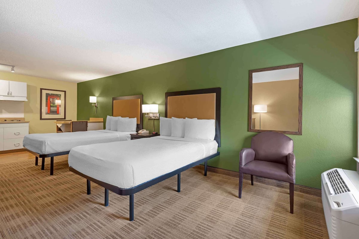Une chambre d’hôtel avec deux lits, une chaise, un bureau et une fenêtre.